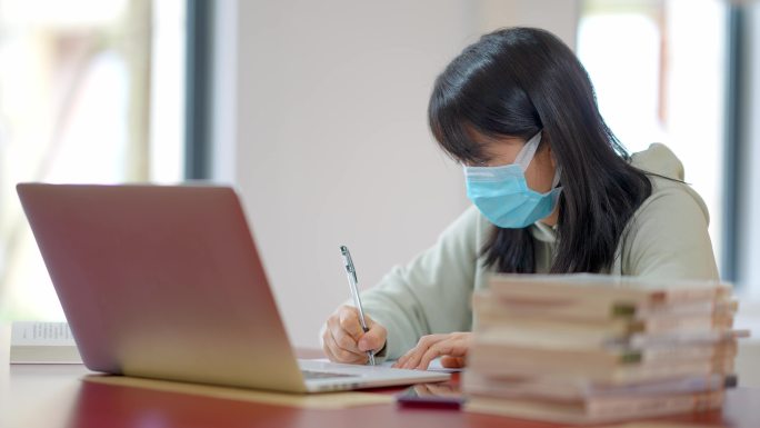 戴口罩年轻女子在图书馆用笔记本学习