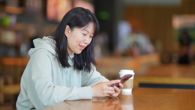 年轻女子在咖啡店使用手机刷朋友圈