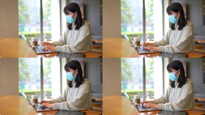 疫情带口罩年轻女子在咖啡店使用笔记本电脑