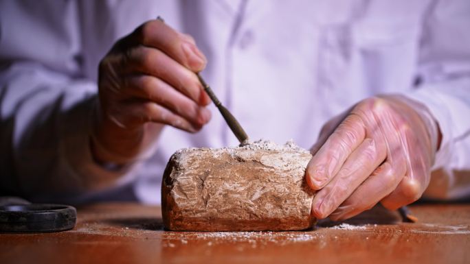 考古人员用洛阳铲和刷子扫除文物上的灰土