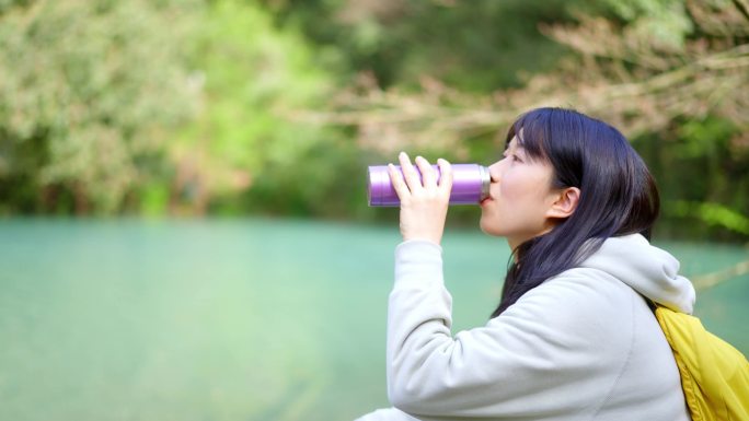 春天年轻女孩郊游踏青歇脚池塘边拿水杯喝水