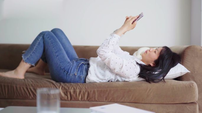 周末年轻女孩躺沙发上玩手机刷手机刷朋友圈
