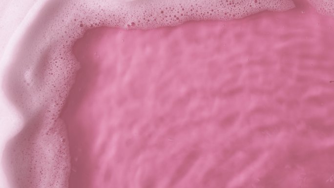 带有泡沫的粉红色水面俯视图。