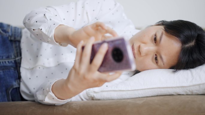周末年轻女孩躺沙发上玩手机刷手机刷朋友圈