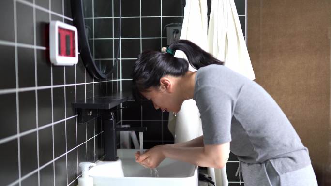 年轻女孩在洗手间打开水龙头在水槽冲洗脸部