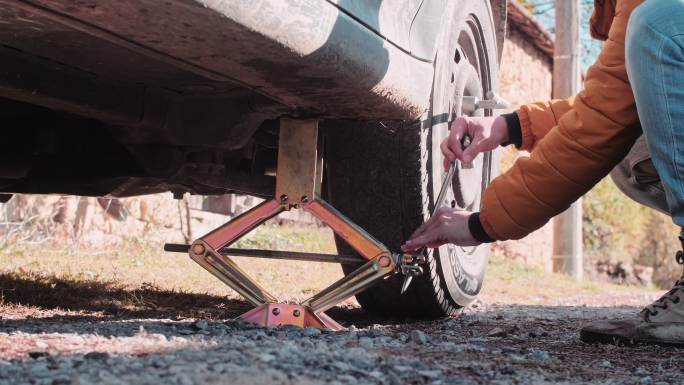 一名女子在乡村道路上更换汽车轮胎。