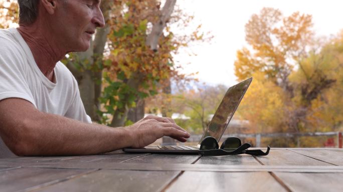 男子在户外野餐桌上使用笔记本电脑