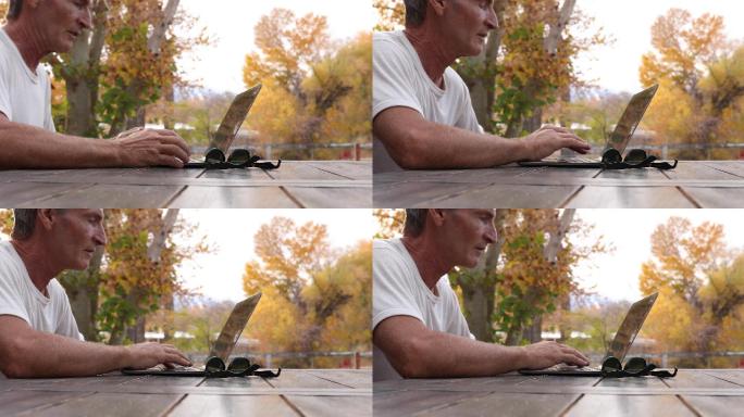 男子在户外野餐桌上使用笔记本电脑