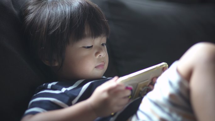 男婴在沙发上用智能手机看动画片