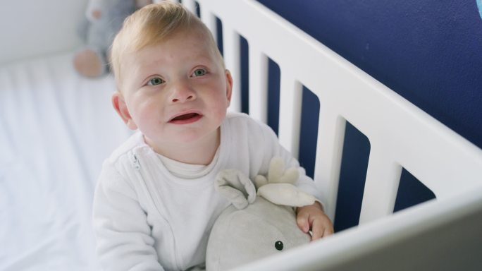 可爱的小男孩在婴儿床上玩泰迪熊