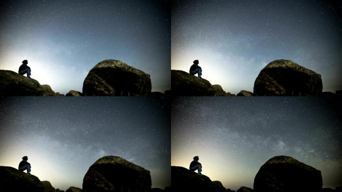 男子坐在岩石上仰望夜空