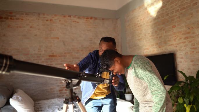 父亲和儿子在家里用望远镜看天空