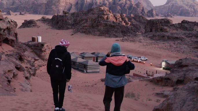黄昏时分，一对男女旅行者在沙漠走向营地