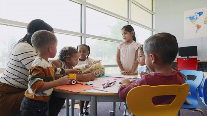 一位教师坐在日托中心的桌子旁教一群幼儿。