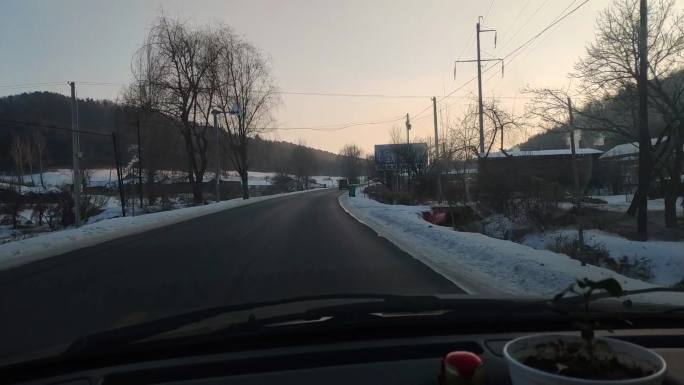 伴着霞光开车行驶在下过雪的村庄道路
