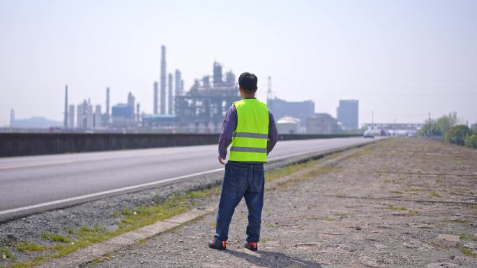 年轻工程技术人员站在路边远望现代石化工厂