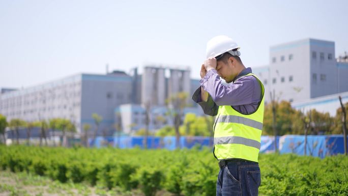 年轻工程技术人员站在工地戴上安全帽看项目