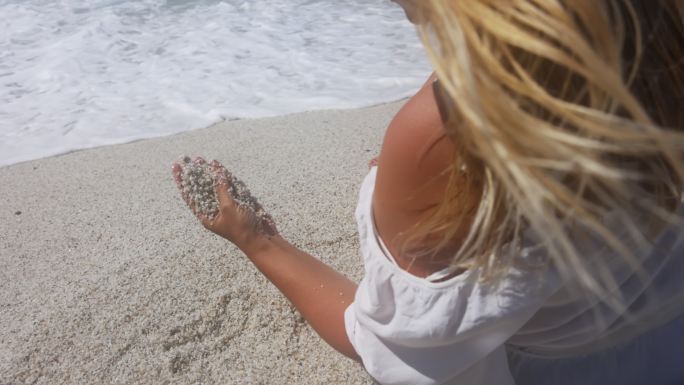 一个女人在海滩上玩沙子的慢镜头。