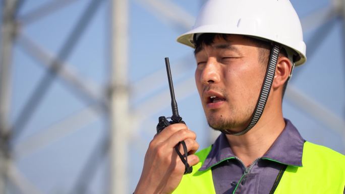 年轻工程技术人员在高压线塔使用对讲机通话