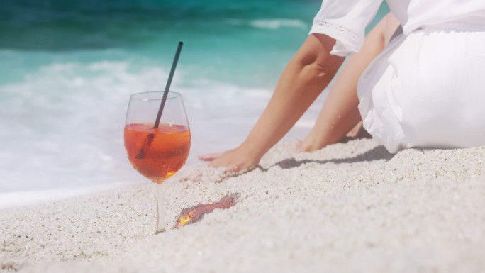 一个女人在海滩上喝鸡尾酒的画面。