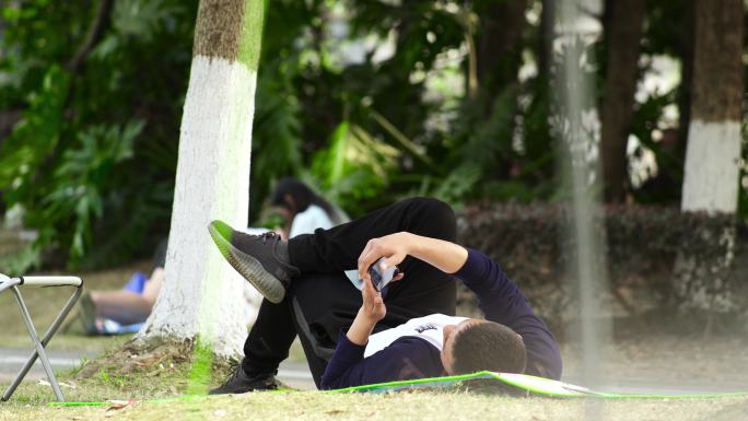 男子躺在公园草坪上玩手机