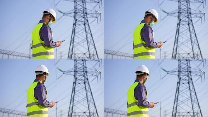 年轻项目技术人员在高压线塔边使用手机通讯
