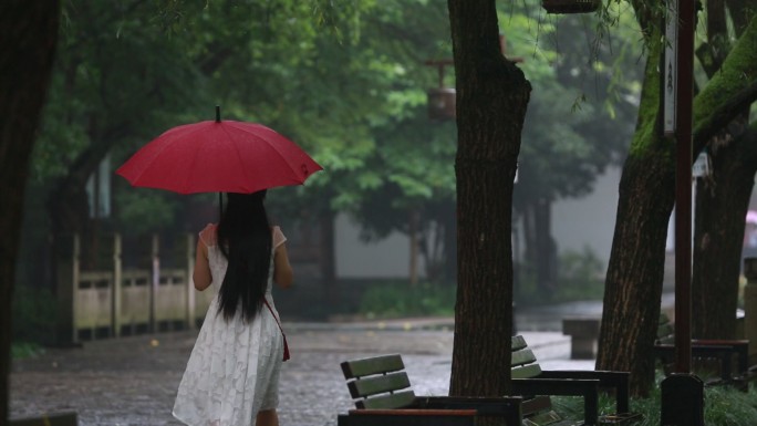 江南雨天穿白裙子女孩戴着红雨伞漫步背影