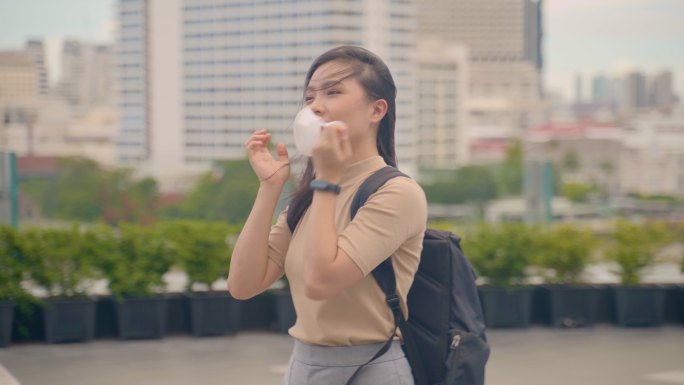 快乐的亚洲女人走在城市街道上，摘下防护口罩。2019冠状病毒疾病的终结已经结束。