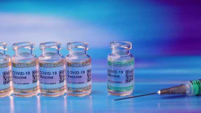 批量2019冠状病毒疾病疫苗瓶蓝色抽象背景。标记SARS-CoV-2以对抗冠状病毒。手戴防护手套拿起