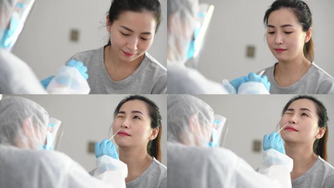 携带PPE的亚裔中国女医生从患者冠状病毒检测中取鼻拭子。防护套间的医务人员正在用拭子进行冠状病毒检测