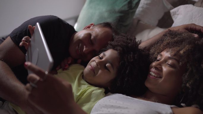 一家人躺在床上，在家里用数字平板电脑观看视频或电影