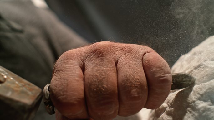 一位男性雕塑家在工作时拿着凿子的那只缓慢的手