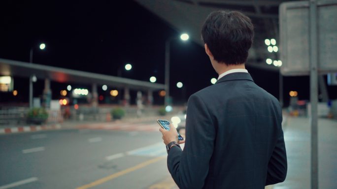 亚洲商人使用智能手机等候出租车或优步，夜晚