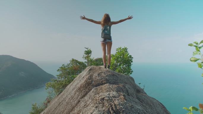 后视图，自由之乐旅行者，29岁的美国裔和西班牙裔女性，在山顶海洋峰会上张开双臂享受旅行假期。张开双臂