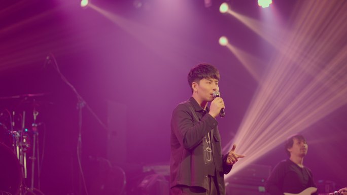 亚洲男歌手带着麦克风在音乐厅的舞台上表演。