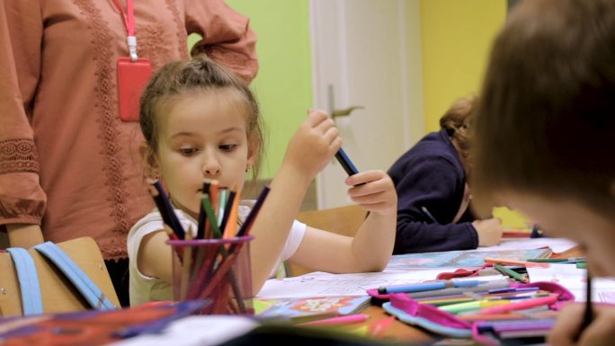 幼儿园学生在课堂上的活动。学龄前儿童一起在书桌上涂色和写字。老师站在他们旁边，给他们暗示和鼓励。带着