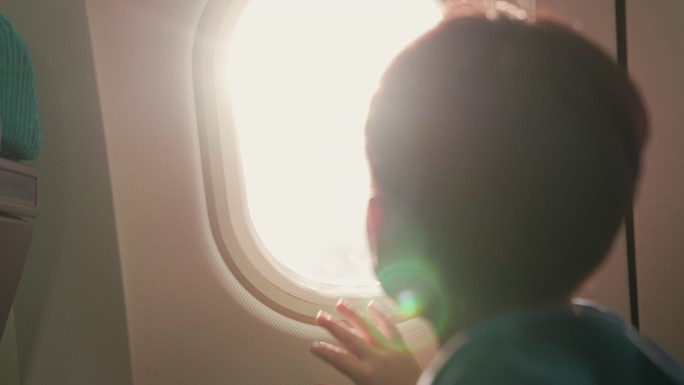 一个男孩坐在窗边的一架商用飞机上，他把手放在窗户上，兴奋得要飞了。从后面拿走。