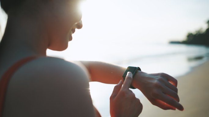 亚洲运动女性使用智能手表监控自己在沙滩上的跑步表现