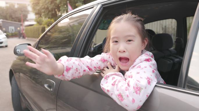 可爱的亚洲小女孩在汽车后座挥手告别