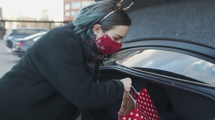 2019冠状病毒疾病流行期间，一名戴着防护面罩的少女在圣诞节购物后把礼物放进车里