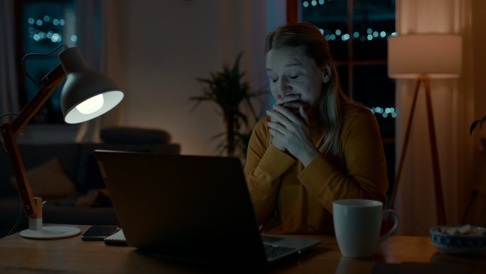 一位精疲力竭的女士晚上在笔记本电脑上工作