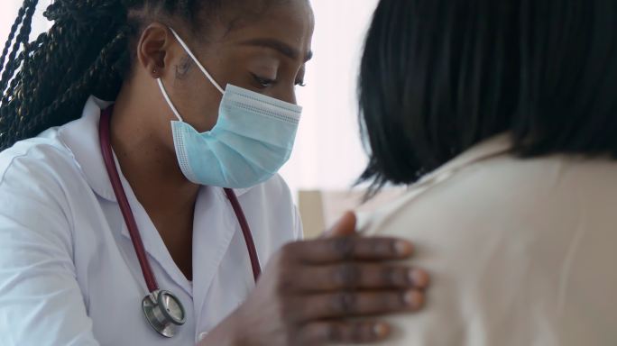 非洲裔女医生儿科医生在看病时与父母交谈和抚摸有助于表达同理心。婴儿患者与住院母亲一起接受医疗检查。医