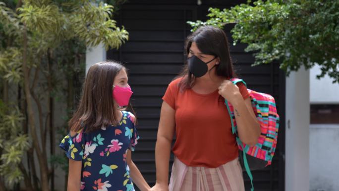 母亲和女儿放学后步行回家——戴着口罩
