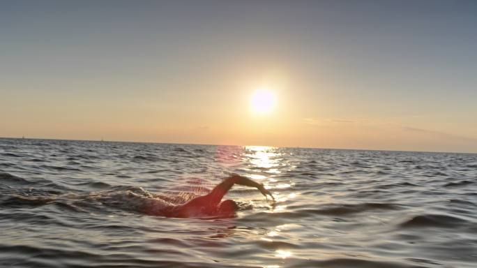 TS男子公开水域游泳运动员日落时在波涛汹涌的大海中游泳