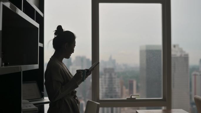 在剪影中，亚洲华裔美女在客厅喝下午茶，看着窗外，靠在桌子上放松