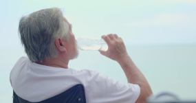 一位亚洲老人坐在海滩上放松。手里提着水瓶，带着清新的感觉喝水。照顾好自己，饮用健康水的理念视频素材