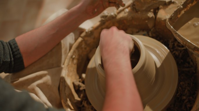 男陶工在陶工的轮子上举起壶壁