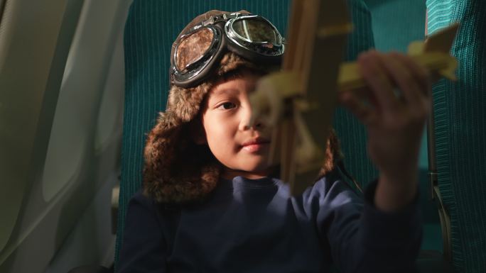 一个男孩坐在商用飞机旁的窗户上。他手里拿着一架玩具飞机，梦想着坐飞机旅行或成为一名飞行员。