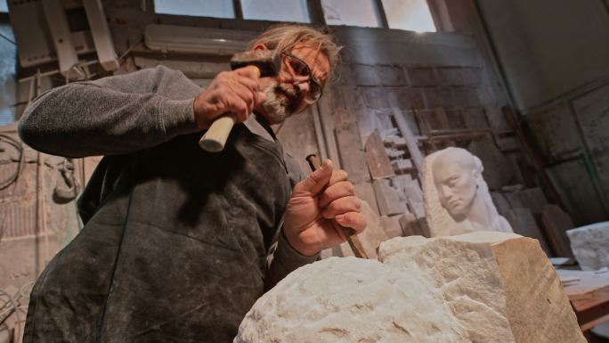 SLO MO男雕刻家凿出白色石雕，颗粒四处飞舞