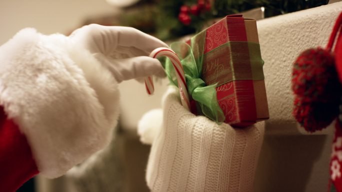 圣诞前夜，圣诞老人戴着手套的手把一根红白相间条纹的糖果手杖放在挂在壁炉架上的圣诞长袜里